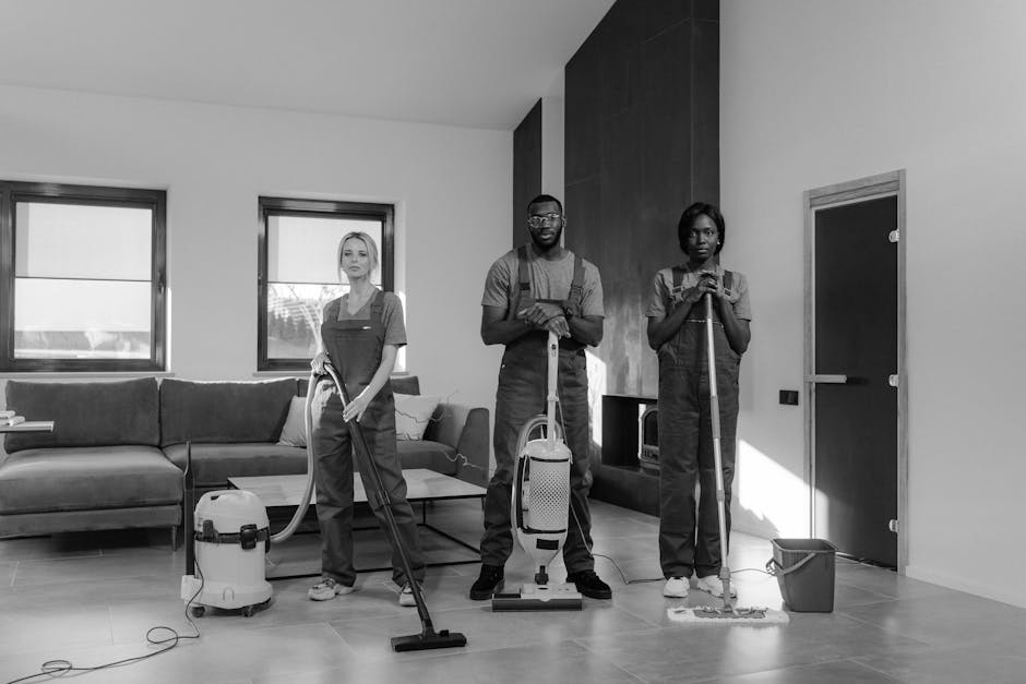 Two professional cleaners from Harringay Cleaners are performing surface cleaning and deep cleaning in a modern living room. One cleaner, on the left, is using a canister vacuum cleaner to clean the w